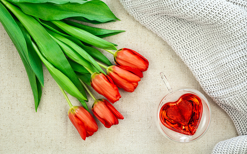 red-tulips-bouquet-next-to-a-heartshaped-tea-glass